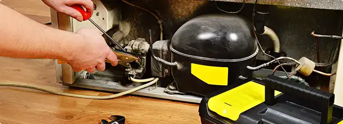 Refrigerator repair technician fixing the compressor and wiring in Pompano Beach, FL