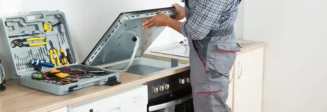 Cooktop repair technician lifting a built-in stovetop for service in Boca Raton, FL