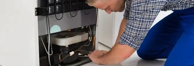 Refrigerator repair technician servicing the compressor and condenser area in Boca Raton, FL