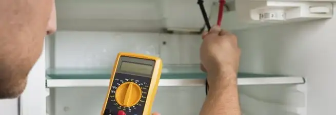 Refrigerator repair technician testing electrical components with a multimeter in Boca Raton, FL