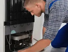 Refrigerator repair technician servicing the compressor and condenser area in Boca Raton, FL
